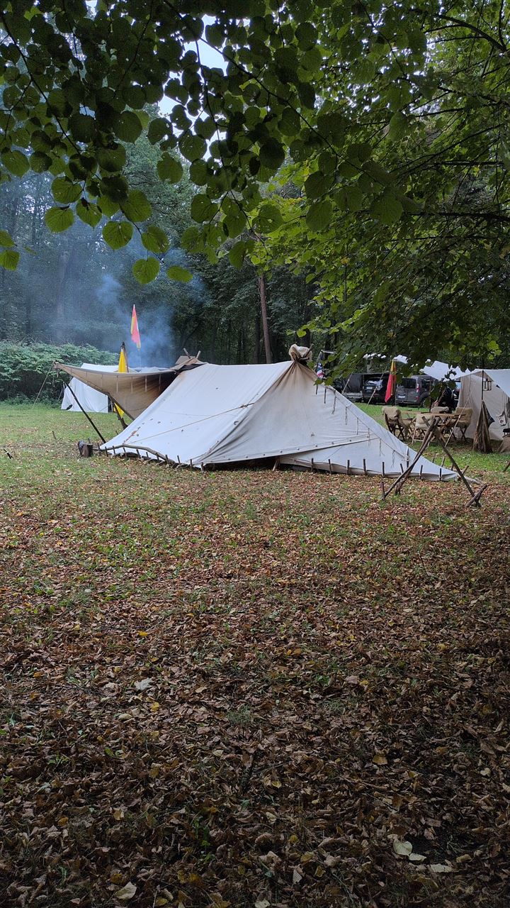 Historisches Zelt auf Laubboden, dahinter Rauch vom Lagerfeuer